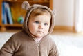 Baby girl with blue eyes wearing brown bear winter overal in sunny bedroom. Newborn child being dressed for an outdoor Royalty Free Stock Photo