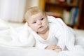 Baby girl with blue eyes wearing white towel or blanket in white sunny bedroom. Newborn child relaxing in bed. Nursery Royalty Free Stock Photo