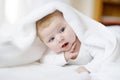 Baby girl with blue eyes wearing white towel or blanket in white sunny bedroom. Newborn child relaxing in bed. Nursery Royalty Free Stock Photo