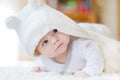 Baby girl with blue eyes wearing white towel or winter overal in white sunny bedroom. Newborn child relaxing in bed Royalty Free Stock Photo