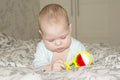 Baby girl boy playing with a rattle on the bed. Little baby looking at a yellow red toy Royalty Free Stock Photo