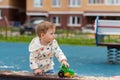 Baby girl boy in a white jacket on a playground outdoor plays with a toy car. Happy Caucasian child 1 year old for a walk in the Royalty Free Stock Photo