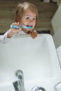 Baby girl in bright bathroom brushing her teeth above the sink