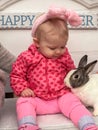 Baby girl in bunny ears petting a live rabbit