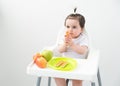 Baby girl in baby chair eating apples and cookies on white background. Baby first solid food