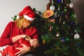 Baby girl disguised as Santa Claus breastfeeding her mother`s chest at Christmas