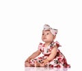 Baby girl in a dress and headband bow sitting barefoot on a white background. Royalty Free Stock Photo