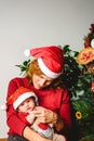 Baby girl dressed as Santa Claus lovingly embraced by her protective mother, family concept at Christmas