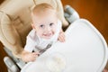 Baby girl eats porridge and looks up, smiling joyfully Royalty Free Stock Photo