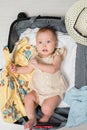 Baby girl with excited and amused expression lies in suitcase with clothes and prepares for summer vacation.