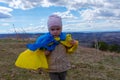 A baby girl with a flag of Ukraine against the hills and Ukrainian nature and blue cloudy sky