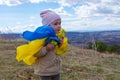 A baby girl with a flag of Ukraine against the hills and Ukrainian nature and blue cloudy sky