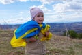 A baby girl with a flag of Ukraine against the hills and Ukrainian nature and blue cloudy sky