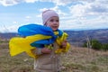 A baby girl with a flag of Ukraine against the hills and Ukrainian nature and blue cloudy sky