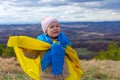 A baby girl with a flag of Ukraine against the hills and Ukrainian nature and blue cloudy sky