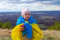 A baby girl with a flag of Ukraine against the hills and Ukrainian nature and blue cloudy sky