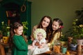 Baby girl in a flower hat on the table with a planting pot and garden plant tools together with her mother and sisters. Home