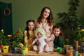 Baby girl in a flower hat on the table with a planting pot and garden plant tools together with her mother and sisters. Home