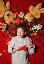 a baby girl with a garland and red hearts in curly hair smiles on a red background and holds a heart in her hands. Royalty Free Stock Photo