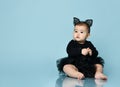 Baby girl in headband in form of cat ears, black bodysuit and tutu, barefoot. She sitting against blue studio background. Close up Royalty Free Stock Photo