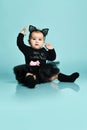 Baby girl in headband in form of cat ears, black bodysuit, tutu and socks. She sitting against blue studio background. Close up Royalty Free Stock Photo