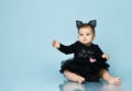 Baby girl in headband in form of cat ears, black bodysuit and tutu, barefoot. She sitting against blue studio background. Close up Royalty Free Stock Photo