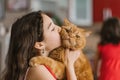 Baby girl holds her pet red British cat in her arms, kisses and sits with him on the couch at home Royalty Free Stock Photo