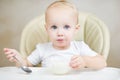Little girl inquiringly looks at the camera, holding a spoon and about to eat porridge Royalty Free Stock Photo