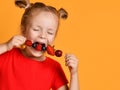 Baby girl kid in red t-shirt holding smelling biting eating fresh berries dessert with cherry strawberry raspberry on skewer Royalty Free Stock Photo