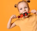 Baby girl kid in red t-shirt holding smelling biting eating fresh berries dessert with cherry strawberry raspberry on skewer Royalty Free Stock Photo