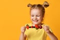 Baby girl kid in t-shirt holding smelling biting eating fresh berries cherry strawberry raspberry on skewer Royalty Free Stock Photo