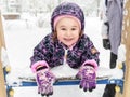 Baby girl lies on playground slide during snowfall. Happy kid having fun plays with snow Royalty Free Stock Photo