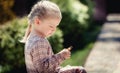 Baby girl with long hair and beautiful dress sits on the doorstep at home and looks at a little doll. Close-up Royalty Free Stock Photo