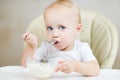 Baby girl looks at the camera, holding a spoon and about to eat porridge Royalty Free Stock Photo