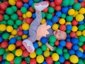 Baby girl lying down in colourful balls and reaching hand to go out Royalty Free Stock Photo