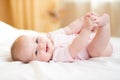 Baby girl lying on white bed and holding her legs Royalty Free Stock Photo