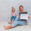 the baby girl and mom sitting on a suitcase against a white brick wall, place under the inscription Royalty Free Stock Photo