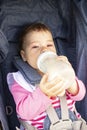 Baby girl 9 months eating from a milk bottle sitting in a stroller, soft focus. A small child independently drinks milk, pink Royalty Free Stock Photo