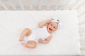 Baby girl 6 months old lies in a crib in the nursery with white clothes on her back and laughs, looks at the camera, baby`s