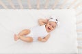 Baby girl 6 months old lies in a crib in the nursery with white clothes on her back and laughs, looks at the camera, baby`s