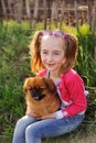 Baby girl with a pekinese sitting on the grass