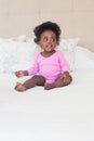 Baby girl in pink babygro sitting on bed Royalty Free Stock Photo