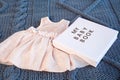 Baby girl pink dres clothes with newborn book album on blue knitting plaid background