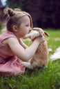 baby girl in a pink dress kiss rabbit in a green meadow in summer. Funny friendship between a child and an animal during Royalty Free Stock Photo