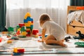 Baby girl playing indoors sitting on floor in playroom at home with constructor. Educational game for baby and toddler Royalty Free Stock Photo