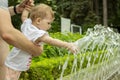 Baby girl playing with water in a fountain in the park. Little baby toddler wets his hands in the fountain. Dad walks with a child Royalty Free Stock Photo