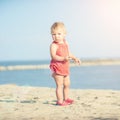 Baby girl in red dress playing on sandy beach near the sea. Royalty Free Stock Photo