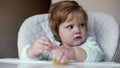 Baby girl sits in high chair with tearful eyes close up in slow motion