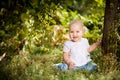 Baby girl sitting on grass in garden under small Apple tree. gardening. Royalty Free Stock Photo