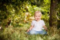 Baby girl sitting on grass in garden under small Apple tree. gardening. Royalty Free Stock Photo